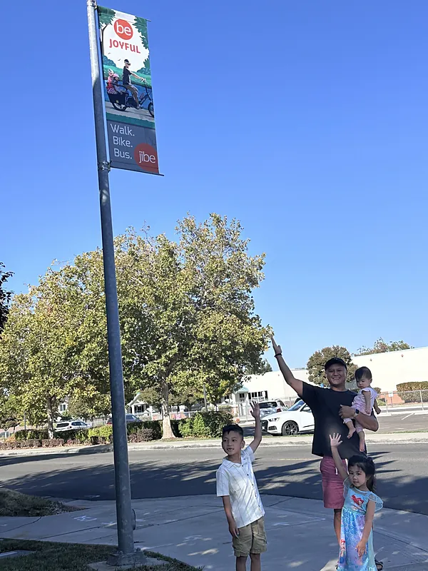 Marvin holding his baby daughter and pointing up at the banner, with his son and older daughter waving