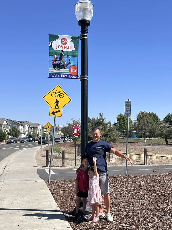Marvin and two of his kids at a bike path crossing under the banner