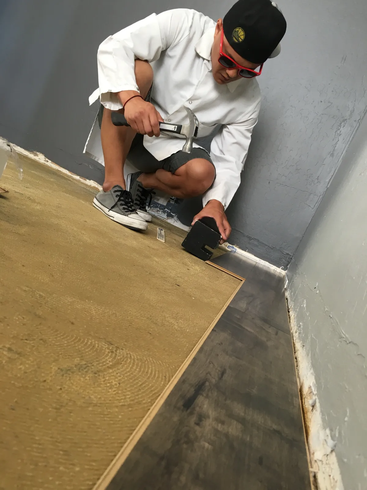 Marvin crouched on the subfloor in a Warriors cap and red sunglasses, hammering the first row of laminate planks into place along the wall