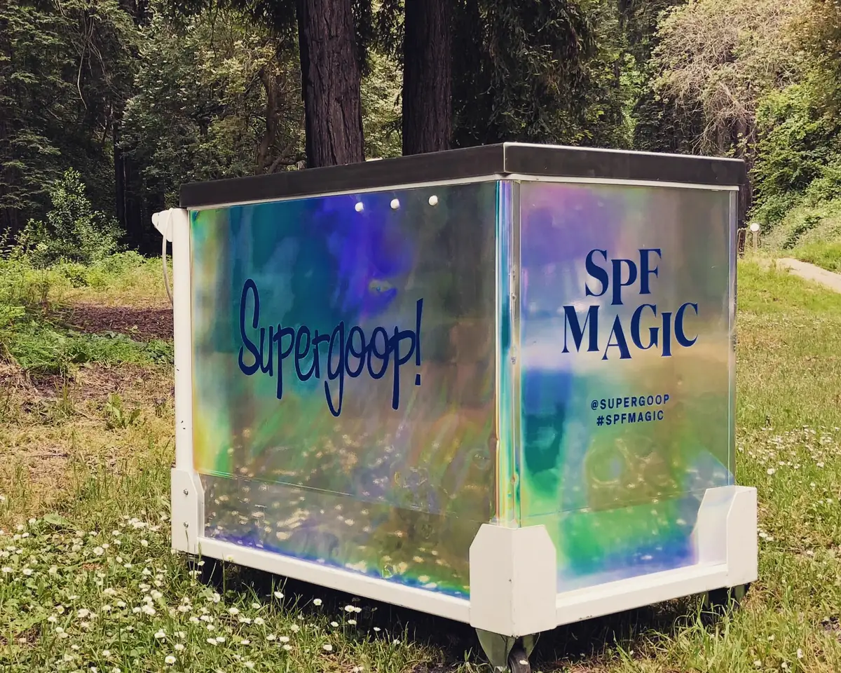A Pop Carts ice cream cart in a holographic Supergoop SPF Magic wrap, parked under redwoods