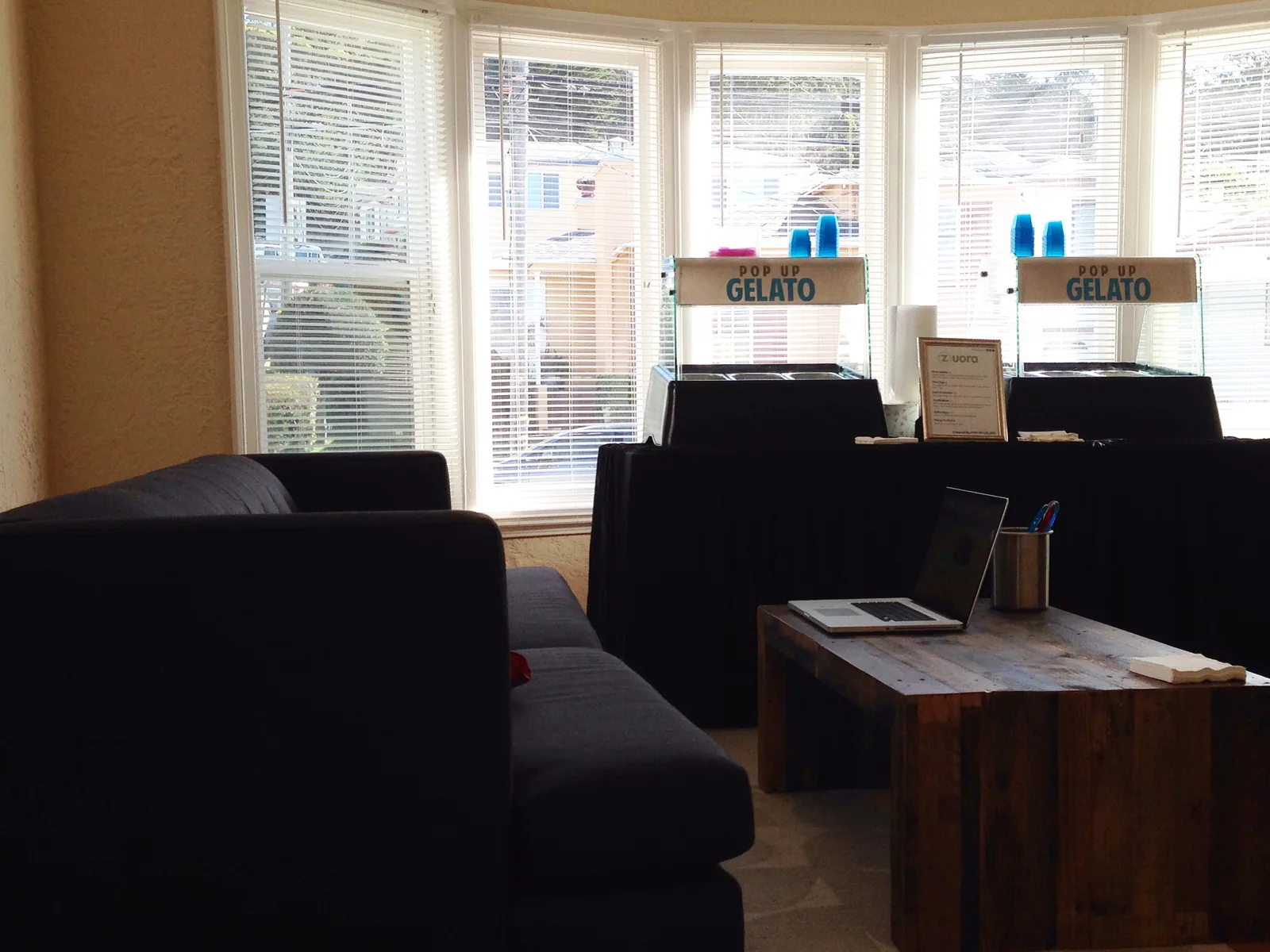 The San Francisco tasting room: two Pop Up Gelato tabletop stations on a black-draped table in a bay window, a couch and reclaimed-wood coffee table in front